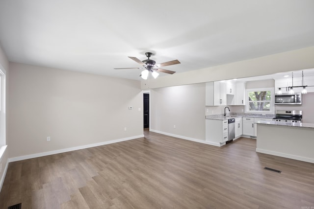 unfurnished living room with a sink, wood finished floors, baseboards, and a ceiling fan