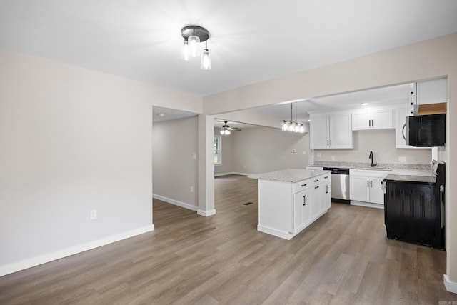 kitchen with stove, black microwave, ceiling fan, a center island, and baseboards