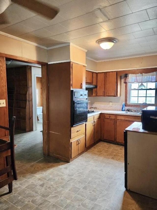 1206 S Main St, Leachville, AR 72438 - kitchen with oven, ornamental molding, light countertops, brown cabinets, and under cabinet range hood
