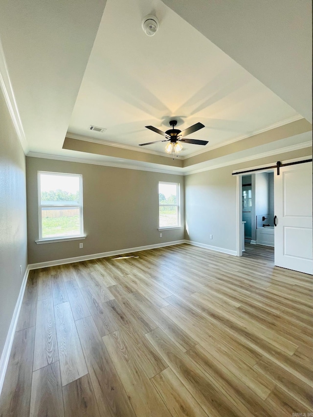 2033 Kaysen Ln, Hensley, AR 72065 - empty room featuring a tray ceiling, a barn door, ornamental molding, baseboards, and light wood-style flooring