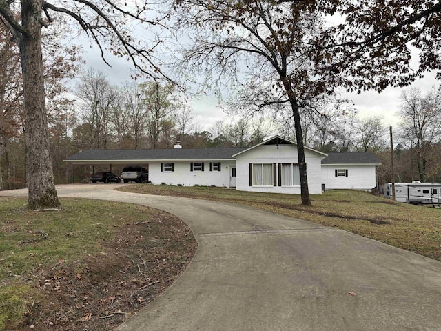 ranch-style home featuring curved driveway, a front yard, a chimney, and a carport