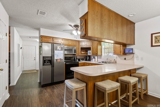 6221 Bray Dr, Benton, AR 72019 - kitchen with appliances with stainless steel finishes, a peninsula, a textured ceiling, brown cabinets, and light countertops