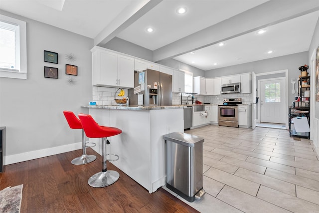 219 W D Ave, North Little Rock, AR 72116 - kitchen featuring stainless steel appliances, tasteful backsplash, white cabinetry, a kitchen bar, and a peninsula