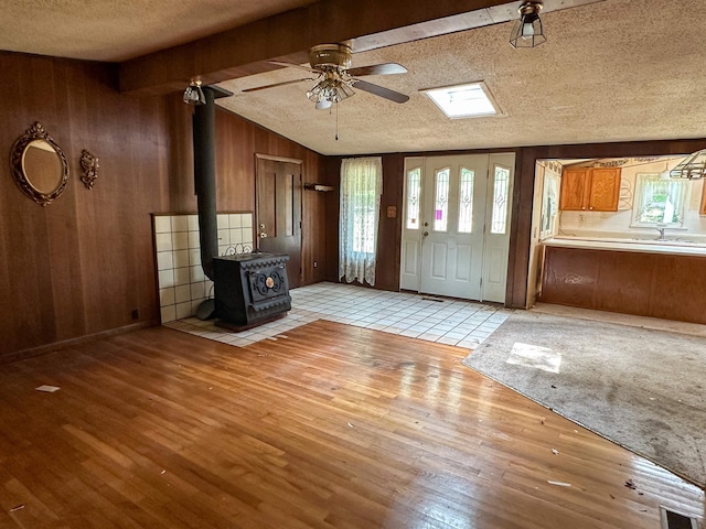 33 W Lakeshore Dr, Cherokee Village, AR 72529 - unfurnished living room featuring light wood-style floors, wooden walls, a textured ceiling, a ceiling fan, and a wood stove