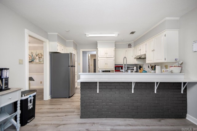 55 Laver Cir, Little Rock, AR 72210 - kitchen featuring freestanding refrigerator, a peninsula, white cabinets, light wood-style flooring, and a kitchen bar