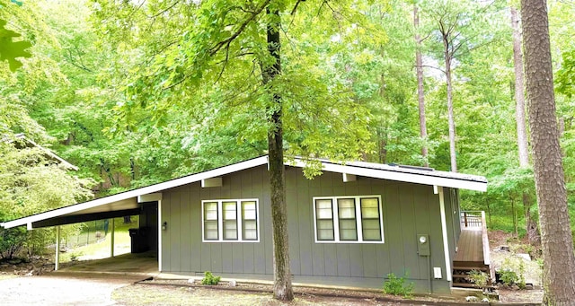 view of front of house featuring an attached carport, a view of trees, and driveway