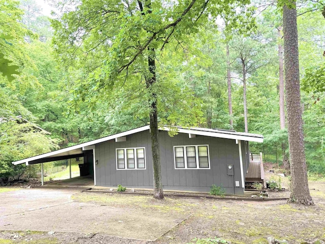 view of front of property with a carport, board and batten siding, concrete driveway, and a forest view