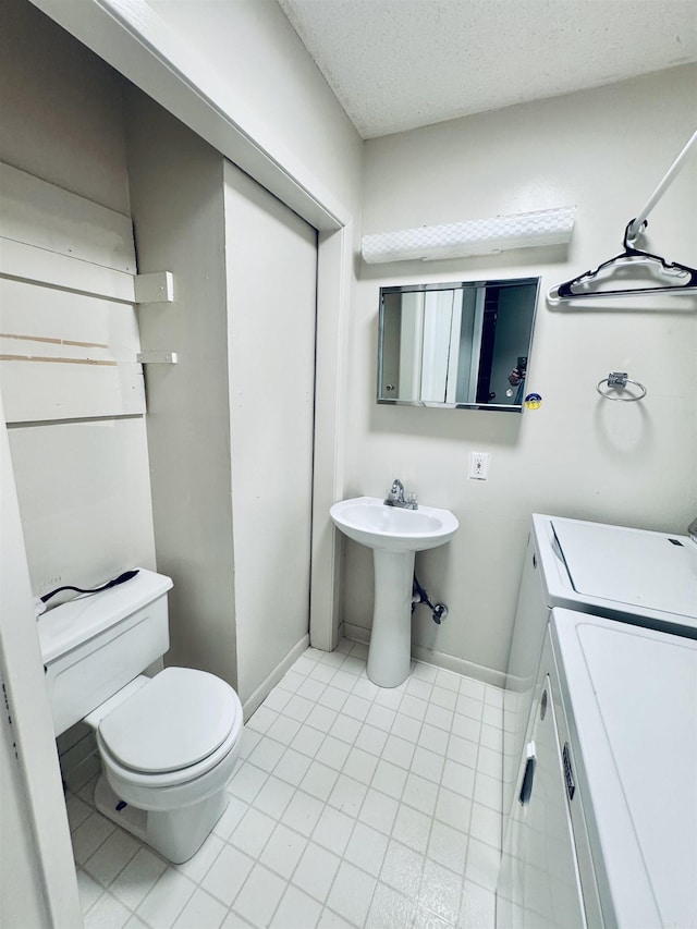 bathroom featuring washing machine and dryer, toilet, baseboards, tile patterned flooring, and a textured ceiling