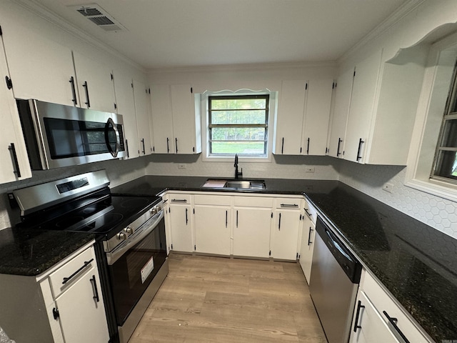 kitchen with appliances with stainless steel finishes, a sink, light wood-style floors, decorative backsplash, and white cabinets