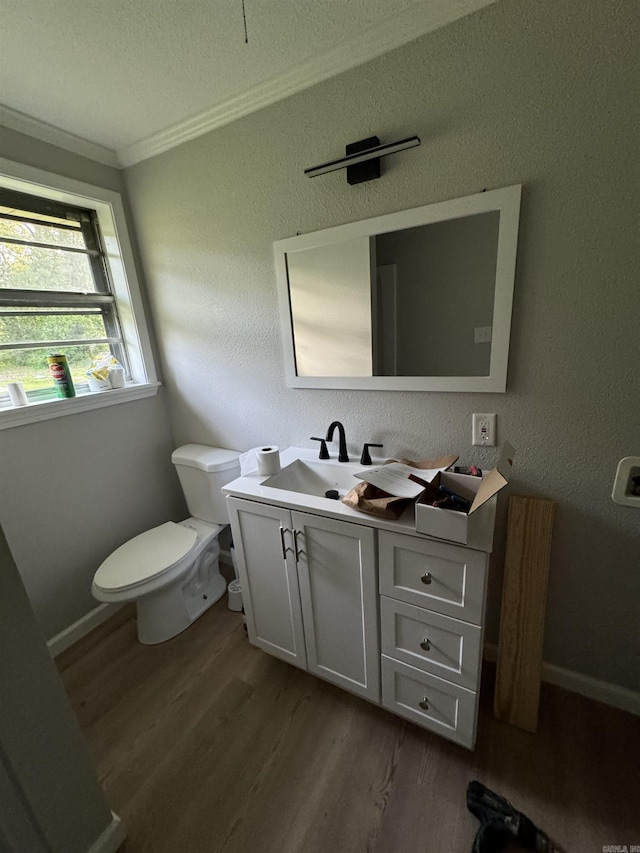 bathroom with vanity, toilet, wood finished floors, crown molding, and baseboards