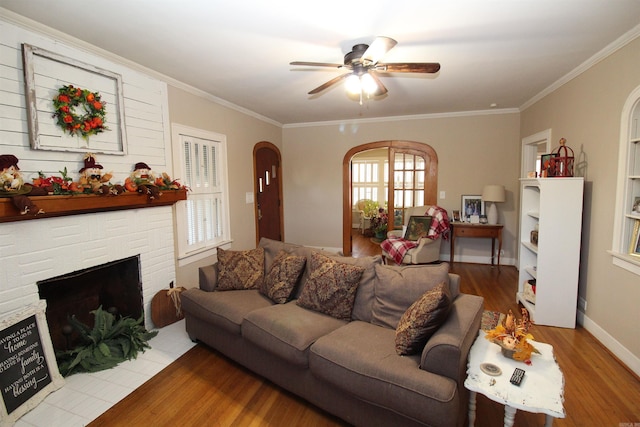 605 School St, Sheridan, AR 72150 - living room featuring wood finished floors, ceiling fan, ornamental molding, a brick fireplace, and arched walkways