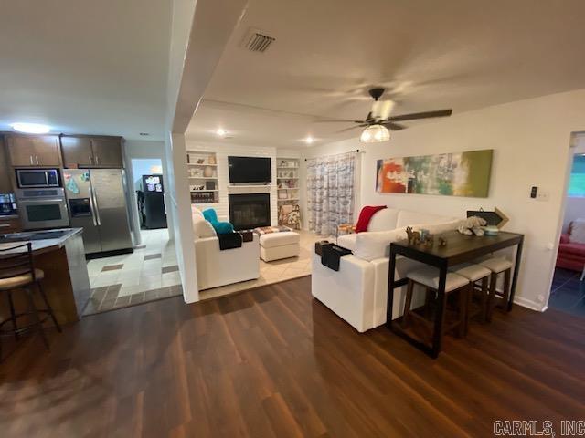 8 Westbrook Cv, Little Rock, AR 72205 - living room with wood finished floors, built in shelves, a ceiling fan, and a glass covered fireplace