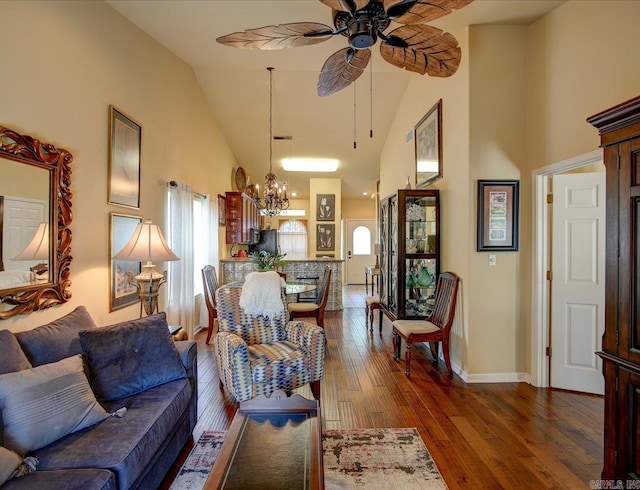 living room with high vaulted ceiling, a chandelier, a ceiling fan, dark wood-type flooring, and baseboards