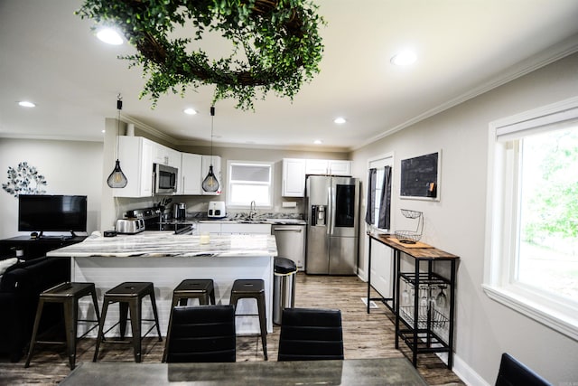 kitchen featuring stainless steel appliances, a peninsula, a sink, ornamental molding, and healthy amount of natural light