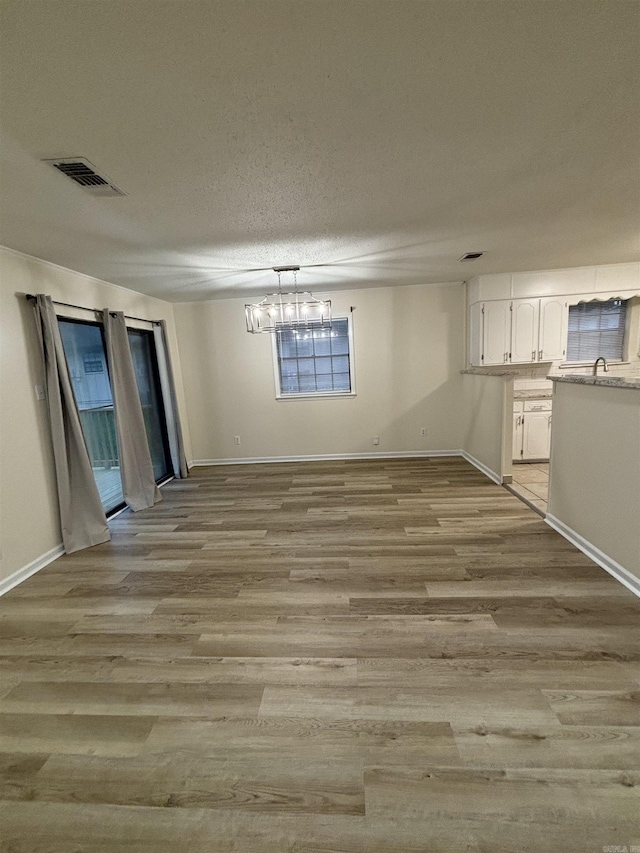 unfurnished dining area with baseboards, light wood-style flooring, a textured ceiling, a sink, and a chandelier
