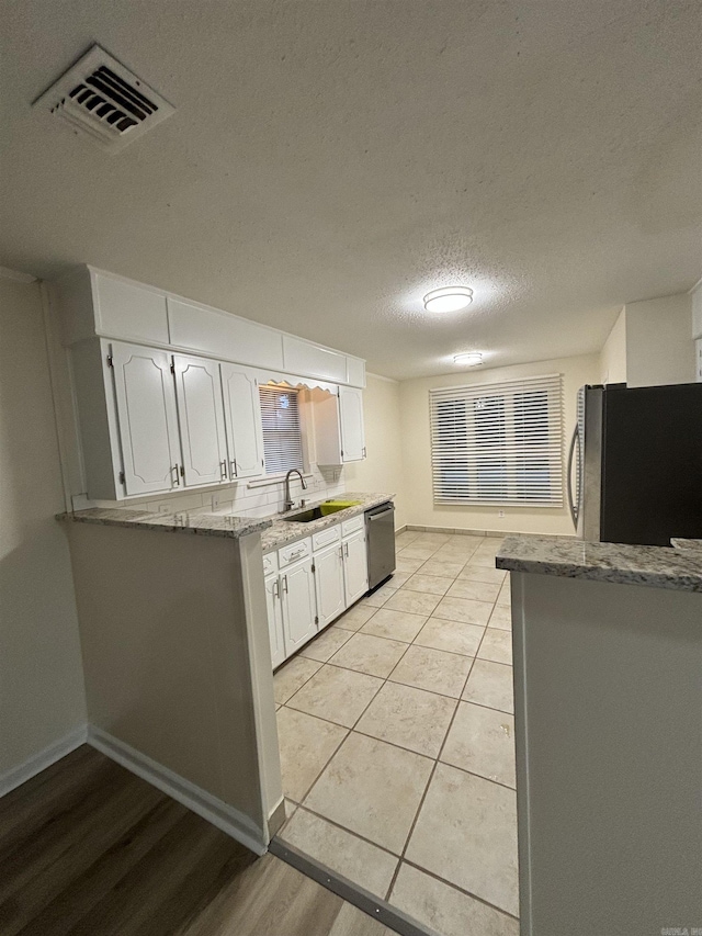 kitchen featuring fridge, dishwasher, white cabinetry, a sink, and a textured ceiling