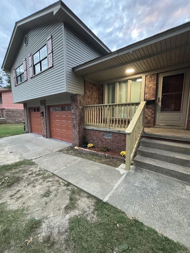 view of property exterior with concrete driveway, an attached garage, a porch, and brick siding