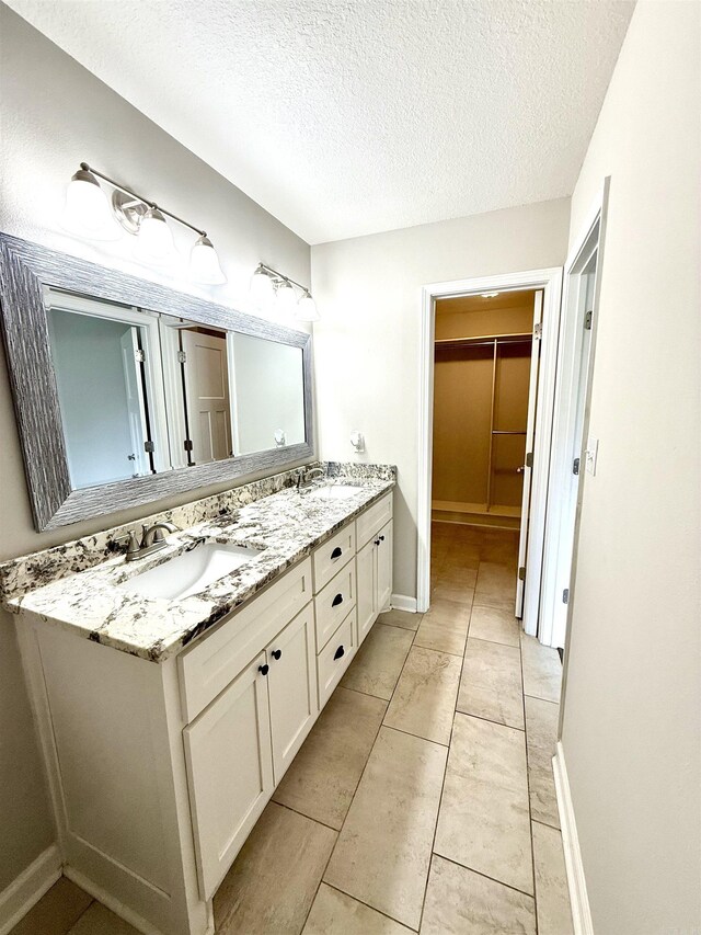 604 Samuel Loyce Dr, Searcy, AR 72143 - bathroom featuring double vanity, a textured ceiling, a walk in closet, baseboards, and tile patterned flooring