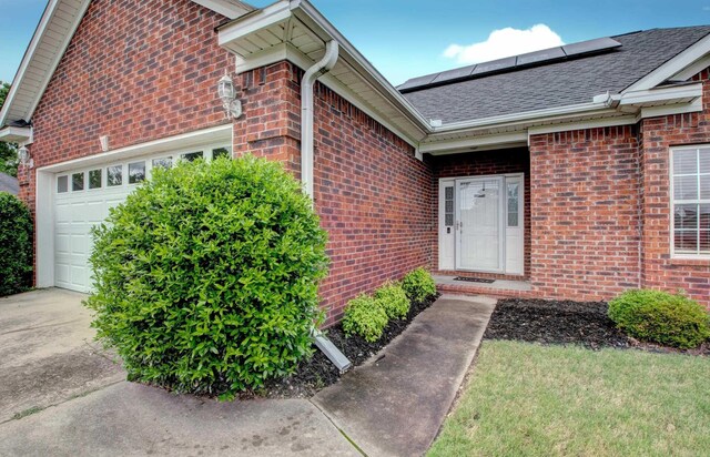 76 Woodridge Dr, Little Rock, AR 72204 - view of exterior entry featuring brick siding, an attached garage, roof mounted solar panels, roof with shingles, and concrete driveway