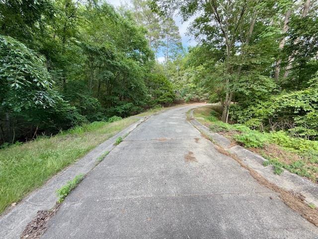 view of asphalt road featuring curbs and a forest view