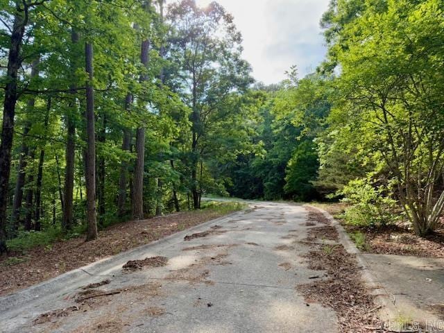 view of asphalt road featuring a forest view and curbs