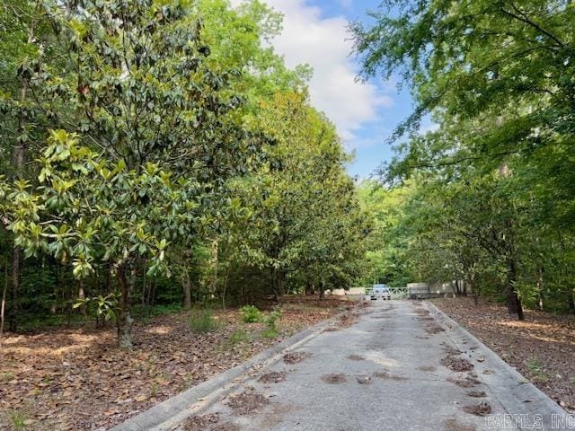 view of asphalt road featuring curbs and a view of trees
