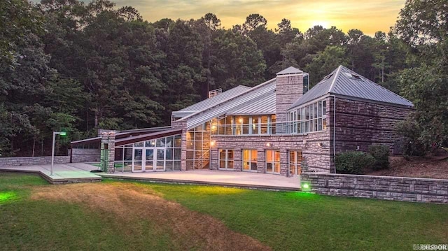 back of property at dusk featuring a lawn, metal roof, a chimney, and stone siding