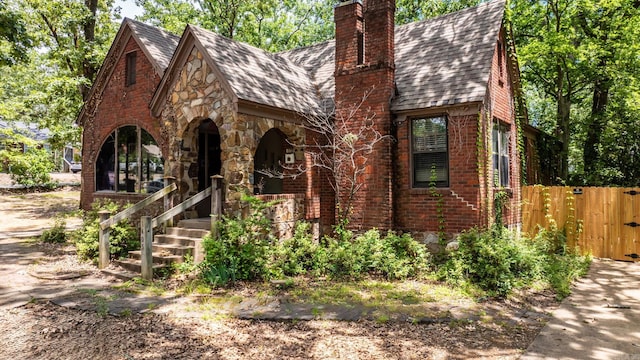 1405 Fair Park Blvd, Little Rock, AR 72204 - tudor-style house featuring a chimney, a porch, a shingled roof, a gate, and stone siding