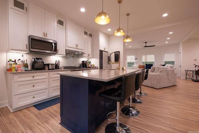 2103 Wolfe St, Little Rock, AR 72202 - kitchen featuring stainless steel microwave, under cabinet range hood, light wood finished floors, decorative backsplash, and open floor plan