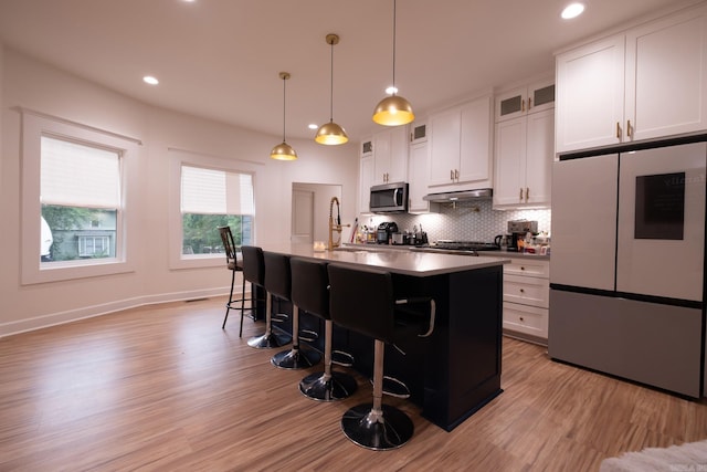 2103 Wolfe St, Little Rock, AR 72202 - kitchen with appliances with stainless steel finishes, under cabinet range hood, a breakfast bar, a center island with sink, and light wood-style floors