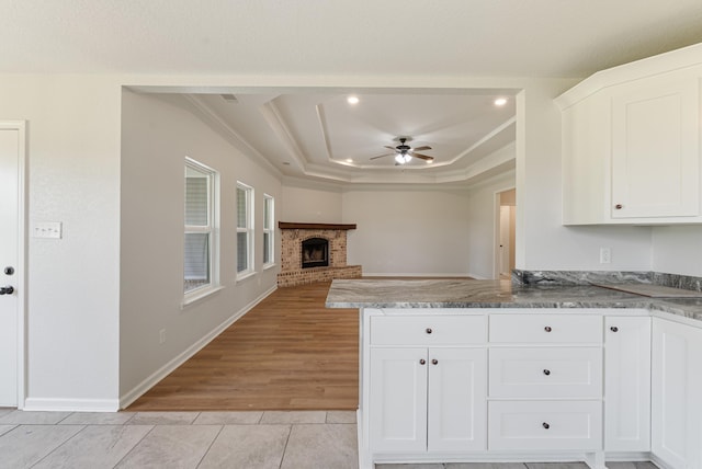 15987 E Miller Sardis Rd, Bauxite, AR 72011 - kitchen with light tile patterned floors, a raised ceiling, white cabinetry, a ceiling fan, and a brick fireplace