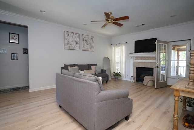 living area featuring a ceiling fan, light wood-style floors, ornamental molding, baseboards, and a tiled fireplace