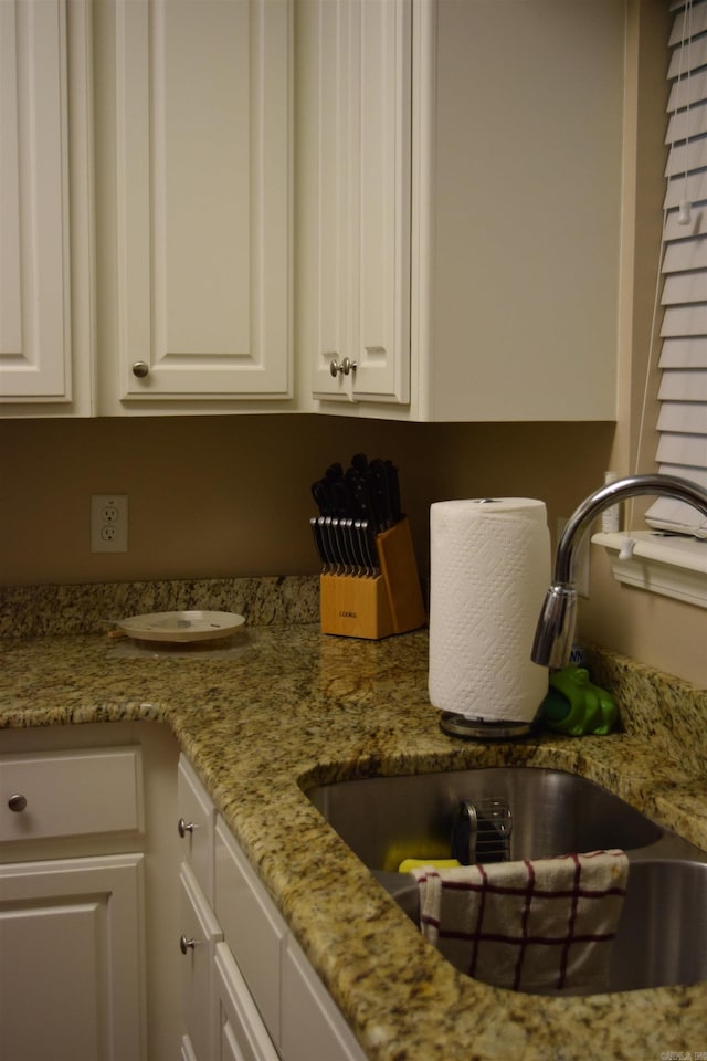 kitchen view of a sink, white cabinetry, and light stone counters