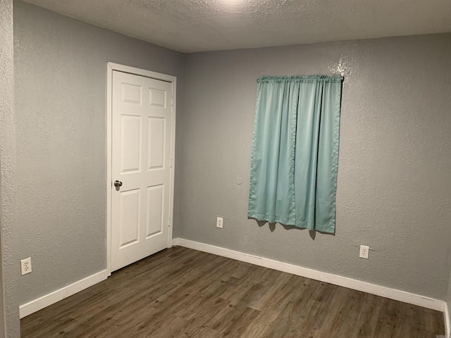 442 S Thornton, Piggott, AR 72454 - unfurnished room with dark wood-type flooring, baseboards, a textured ceiling, and a textured wall