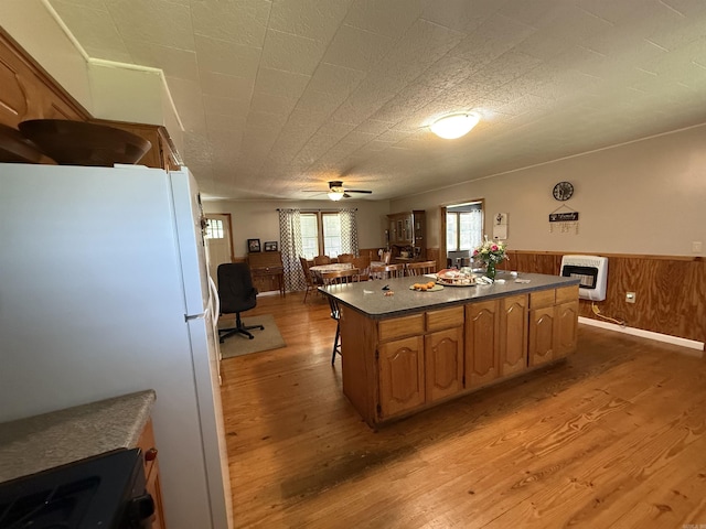 221 N Garfield Ave, Piggott, AR 72454 - kitchen featuring light wood-type flooring, a center island, dark countertops, freestanding refrigerator, and a wainscoted wall