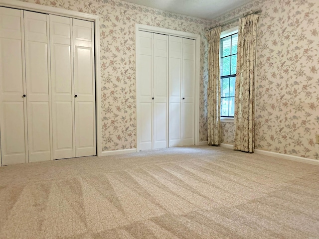 unfurnished bedroom with wallpapered walls, carpet floors, multiple closets, and baseboards