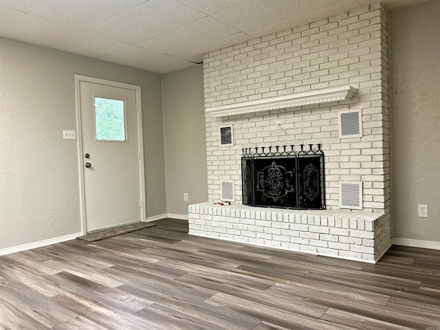 unfurnished living room with wood finished floors, a brick fireplace, baseboards, and a paneled ceiling