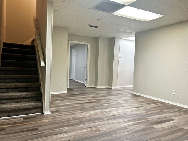finished below grade area with wood finished floors, stairway, a drop ceiling, a textured wall, and baseboards