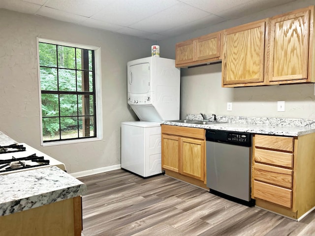 kitchen featuring dishwasher, stacked washer and clothes dryer, a sink, light wood finished floors, and a drop ceiling