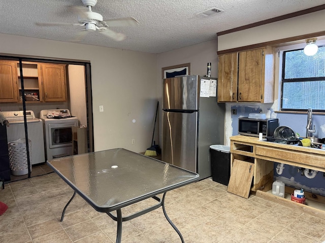 kitchen with freestanding refrigerator, brown cabinets, ceiling fan, a textured ceiling, and washing machine and dryer