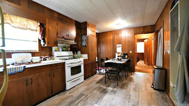 911 Gillham, Mena, AR 71953 - kitchen with white gas stove, under cabinet range hood, wood walls, light countertops, and a heating unit