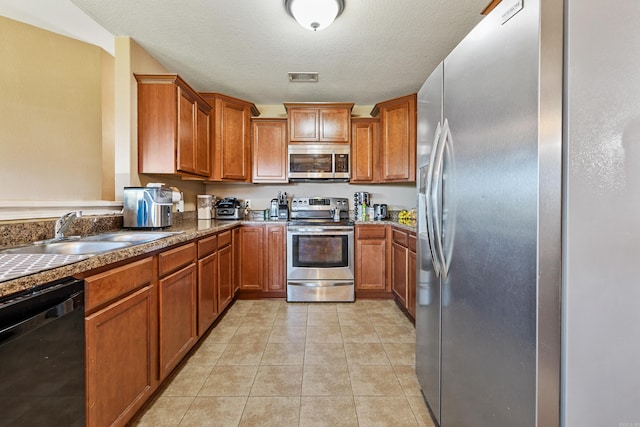 kitchen featuring stainless steel appliances, a sink, brown cabinets, light tile patterned flooring, and a textured ceiling