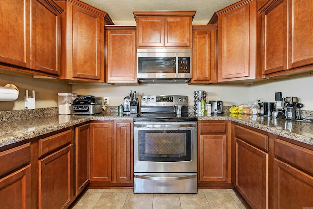 kitchen featuring stainless steel appliances, dark stone counters, light tile patterned floors, brown cabinetry, and a textured ceiling