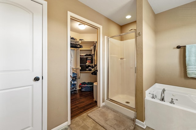 full bathroom with a shower stall, a bath, a spacious closet, tile patterned floors, and baseboards