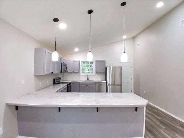 kitchen with appliances with stainless steel finishes, gray cabinetry, a peninsula, dark wood finished floors, and a breakfast bar area
