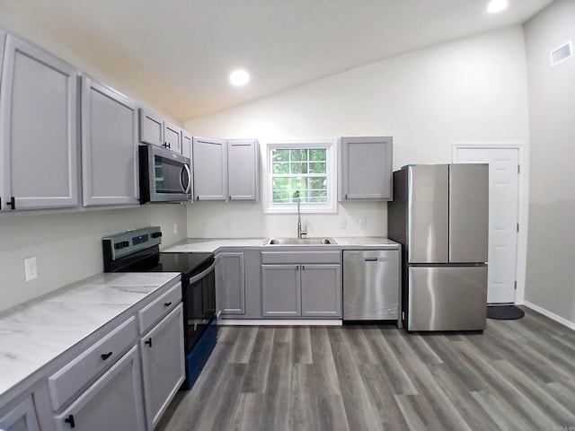 kitchen featuring stainless steel appliances, a sink, gray cabinetry, vaulted ceiling, and dark wood-style floors