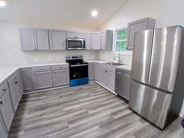 kitchen featuring appliances with stainless steel finishes, a sink, gray cabinetry, recessed lighting, and lofted ceiling