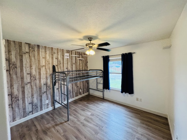 112 Seminole Cir, Austin, AR 72023 - unfurnished bedroom featuring wood walls, wood finished floors, baseboards, a textured ceiling, and a ceiling fan