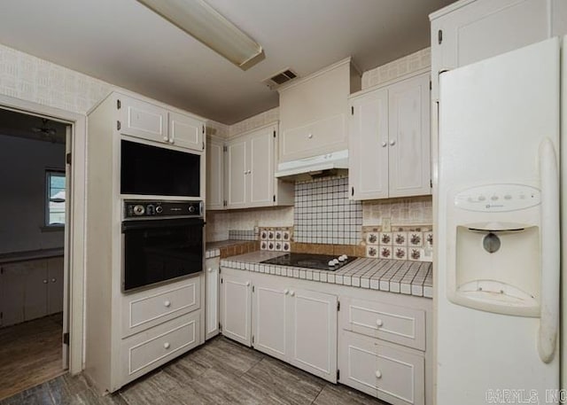 kitchen with black appliances, white cabinets, under cabinet range hood, and decorative backsplash