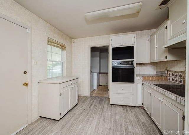 kitchen featuring black appliances, light wood-type flooring, under cabinet range hood, and white cabinets
